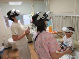 病室でVRゴーグルを装着し，患者さんと保護者，病棟保育士が一緒に交流イベントに参加する様子